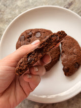 Chocolate chip cookie held by a hand with more cookies on a plate in the background. – thumbnail 1