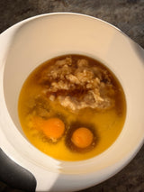 White bowl with brown liquid, egg yolks, and pieces of meat on a dark surface – thumbnail 4