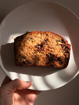 Loaf of banana bread on a white plate held by a hand. – thumbnail 2