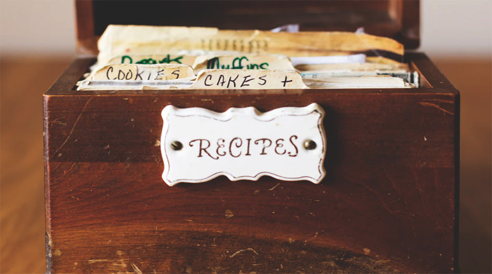 Wooden recipe box with card labels inside, on a wooden surface.